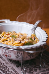 Photo of a fresh hot delicious italian fussili pasta with sea mussels, black olives, red chilli peppers and fresh greens in a white porcelain marmite 