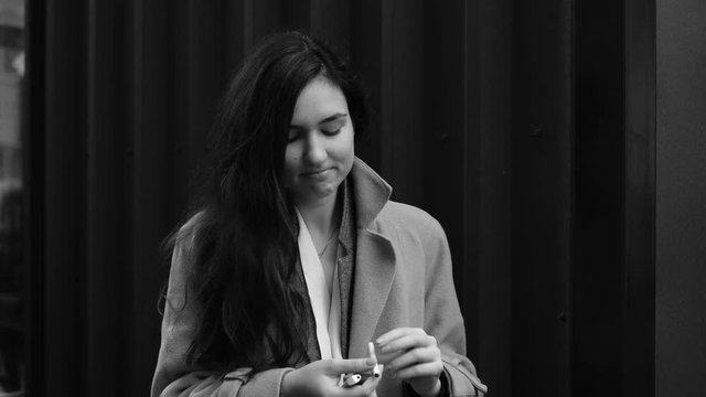 Sad young woman in a coat lights up a cigarette and smokes shooted in black and white