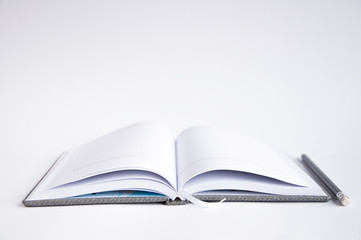 open notebook on the table. On the notebook is a black pencil. On a white background
