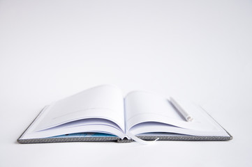 open notebook on the table. On the notebook is a pen or marker. On a white background