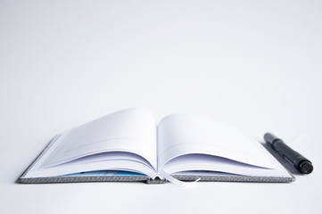 open notebook on the table. On the notebook is a pen or marker. On a white background