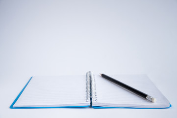 open notebook on the table. On the notebook is a black pencil. On a white background