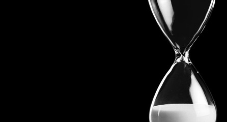 Sand running through the bulbs of an hourglass on black background