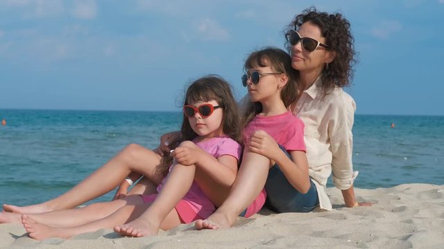 Family on vacation. Cute little girls with their mother are sitting on the sand on the seashore.