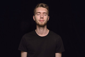 Obraz premium Close up portrait of young man isolated on black studio background. Photoshot of real emotions of male model with closed eyes. Thoughtful. Facial expression, human nature and emotions concept.
