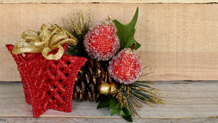 red glitter gift box shape with a gold glitter bow next to pine cone and fruit spray standing on a wood background with copy space