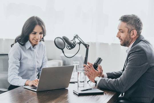 smiling radio host using laptop while interviewing businessman in radio studio