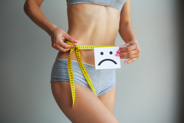 Diet concept. Hands measuring waist with a tape. Slim and healthy woman at her home