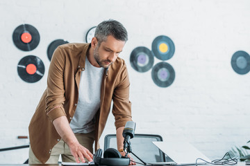 handsome radio host looking at notebook while standing at workplace in radio studio