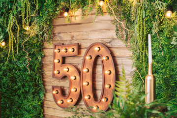Photo zone made of natural wood on the anniversary, decorated with fresh greenery and a garland. The inscription "50".