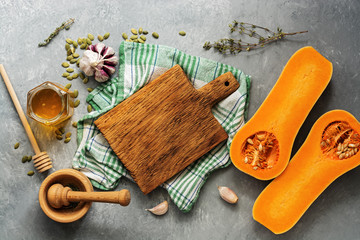 Fototapeta na wymiar Raw pumpkin or butternut squash, empty cutting board, herbs, honey on a gray background. Top view, flat lay, copy space.