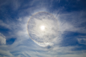 Obraz premium The halo appeared in the blue sky around the sun during the day. A halo-optical phenomenon, a glowing ring around a light source. Cloudscape, nature, summer.
