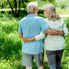 cheerful retired man hugging happy senior wife in green park