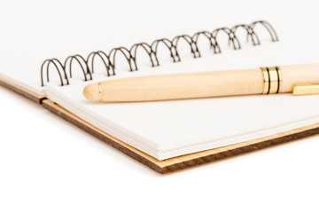 The handle in a wooden case with a cap lies on an empty sheet of an open notebook with a wooden cover and sheets of recycled paper . Close-up.