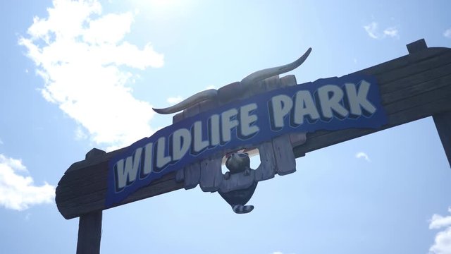 Establishing shot of a zoo wildlife refuge sign against blue sky