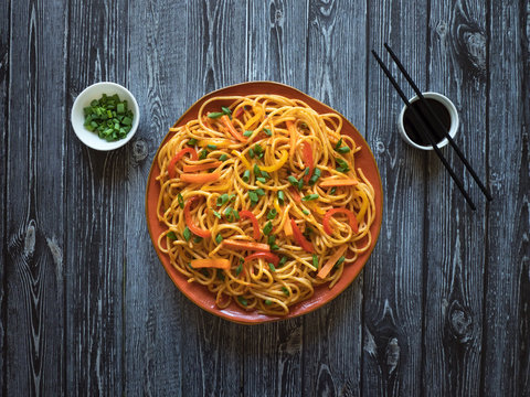 Schezwan Noodles with vegetables in a plate on a wooden table. Top view. Hakka Noodles is a popular Indo-Chinese recipes