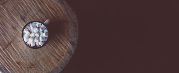 An old enamel Christmas mug filled with hot chocolate and marshmallows stands on the round section of the tree. Top view, copy space.