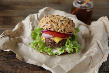 Close-up Big sandwich - hamburger with beef, tomatoes, onions, cheese, lettuce and a sesame bun with coca-cola in a glass on a paper on a wooden rustic board. Fast food dinner concept.