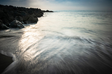 beautiful sandy scenic beach in sunset, with rocky breakwater in long exposure in basque country,...