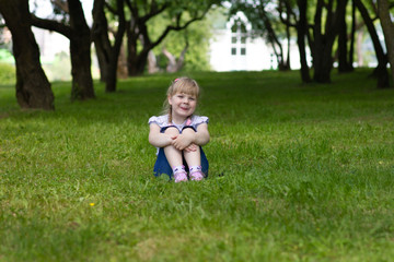Sweet, happy little girl sitting on a grass in a park