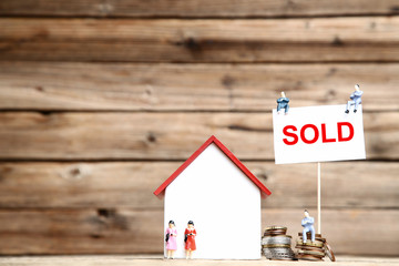 Wooden house model with miniature people and coins on brown background