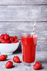 Smoothie in glass with strawberries on grey wooden table