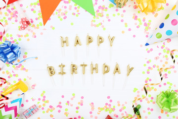 Happy Birthday candles with party decorations on white wooden table