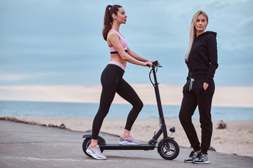 Two attractive sportive womens have nice time at the seaside with electro scooter.