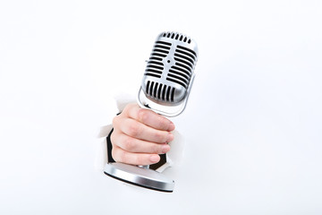 Hand holding microphone from white torn paper