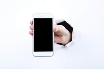 Hand holding smartphone from white torn paper