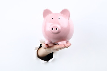 Hand holding pink piggybank from white torn paper