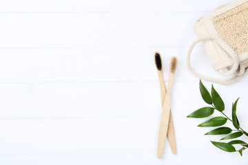 Bamboo toothbrushes with washcloth and green leafs on white wooden table