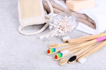 Bamboo toothbrushes with washcloth, cotton sticks and towels on grey background