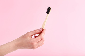 Bamboo toothbrush in female hand on pink background