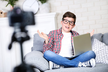 Young boy with laptop sitting on sofa and records video