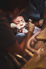 Little scared boy got an remedy via syringe by diligent dentist.