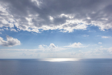 Background image of sky with clouds, sea, reflection of light on water, sun behind clouds