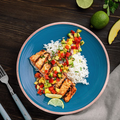 Grilled fillet of salmon with rice garnish and exotic fruit sauce made of mango, avocado, pepper and onion on a rustic table. Top view shot above.