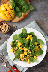Diet menu, Vegan food. Healthy salad with spinach, mango, pecan and vinaigrette dressing on a dark stone table.