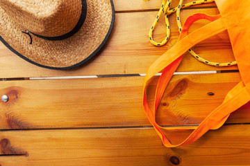 A wicker hat, a yellow rope, and an orange tote bag are laying on a wooden surface