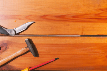 A pocket knife, screwdriver, and a hammer are laying on a wooden surface