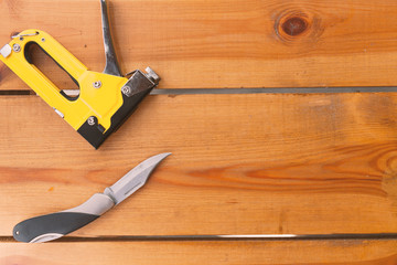 An automatic staple gun and a pocket knife are laying on a wooden surface