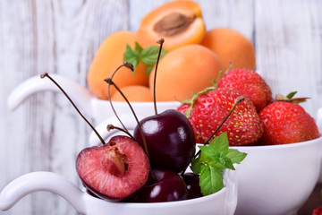 Cherries, strawberries and apricots in little white cups on the wooden table