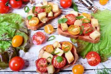 Bruschetta with cherry tomatoes and cheese topped with greenery on the white wooden table