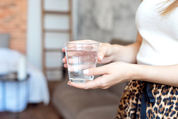 Girl in white top and skirt with a trendy print holds a glass of clean water to maintain the body's...