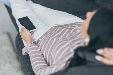 selective focus of young woman lying on sofa and holding smartphone with blank screen