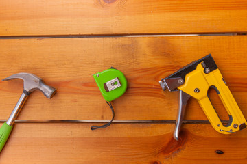 A hammer, measuring tape, and a staple gun are laying on a wooden surface