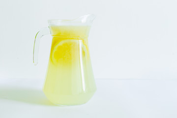 Big glass pitcher with ice cold lemonade with slices of lemon on a white background – Sweet and healthy drink full of vitamins – Refreshing beverage for hot summer days with copy space