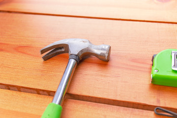 A hammer and a measuring tape are laying on a wooden surface