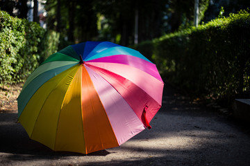 Umbrella with rainbow colors placed in the sun on a sidewalk in the park – Multicolored waterproof equipment used on rainy days